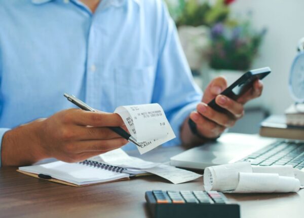 Man using smartphone and holding bills checking for cost in the home office,Start up counting finance.tax system.
